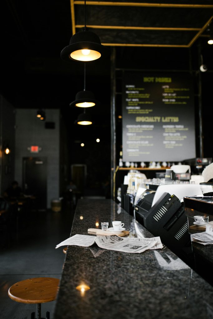 A cozy cafe in Greensboro featuring a granite bar with a cup, newspapers, and hanging lamps.